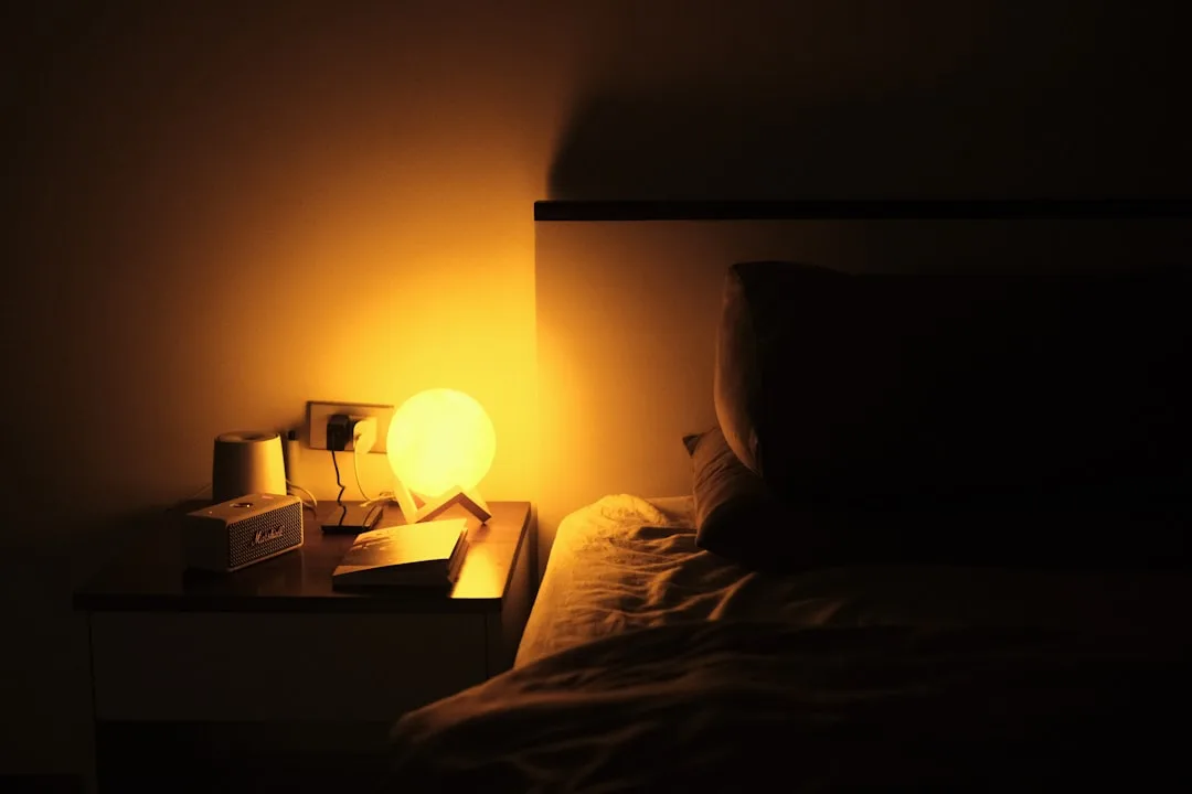 Warm amber globe lamp glowing on bedside table beside open book and Marshall speaker in dark bedroom