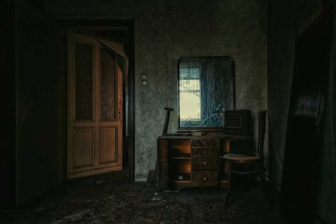 Dark abandoned room with aged wallpaper, antique dresser and mirror showing how dark wall tones create moody atmosphere