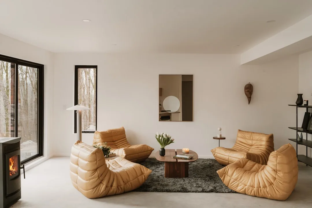 Warm minimalist living room with camel leather Togo chairs, wood coffee table, dark rug, and white walls with fireplace