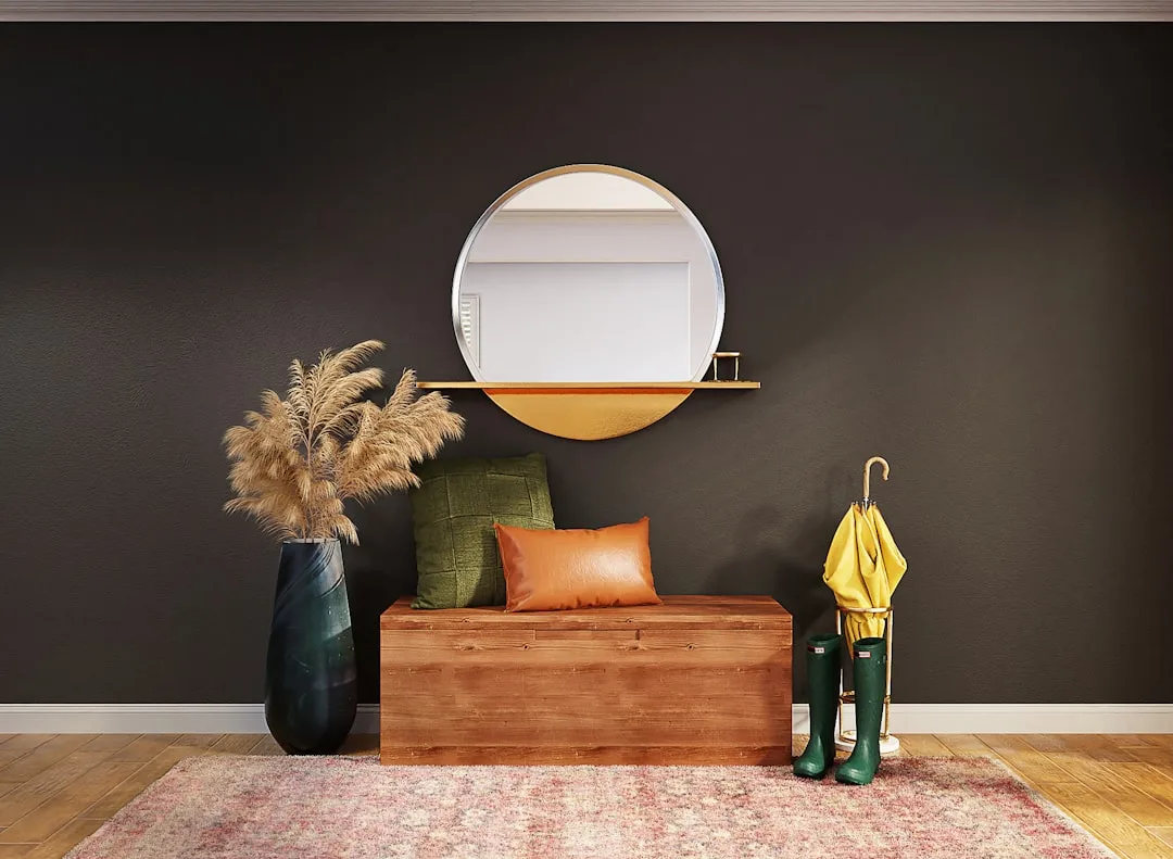 Styled entryway with round gold mirror, wooden storage bench, pampas grass vase, green rain boots and yellow umbrella