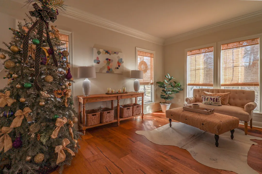 Farmhouse living room with decorated Christmas tree in gold, green and purple with warm neutral tones and wood floors