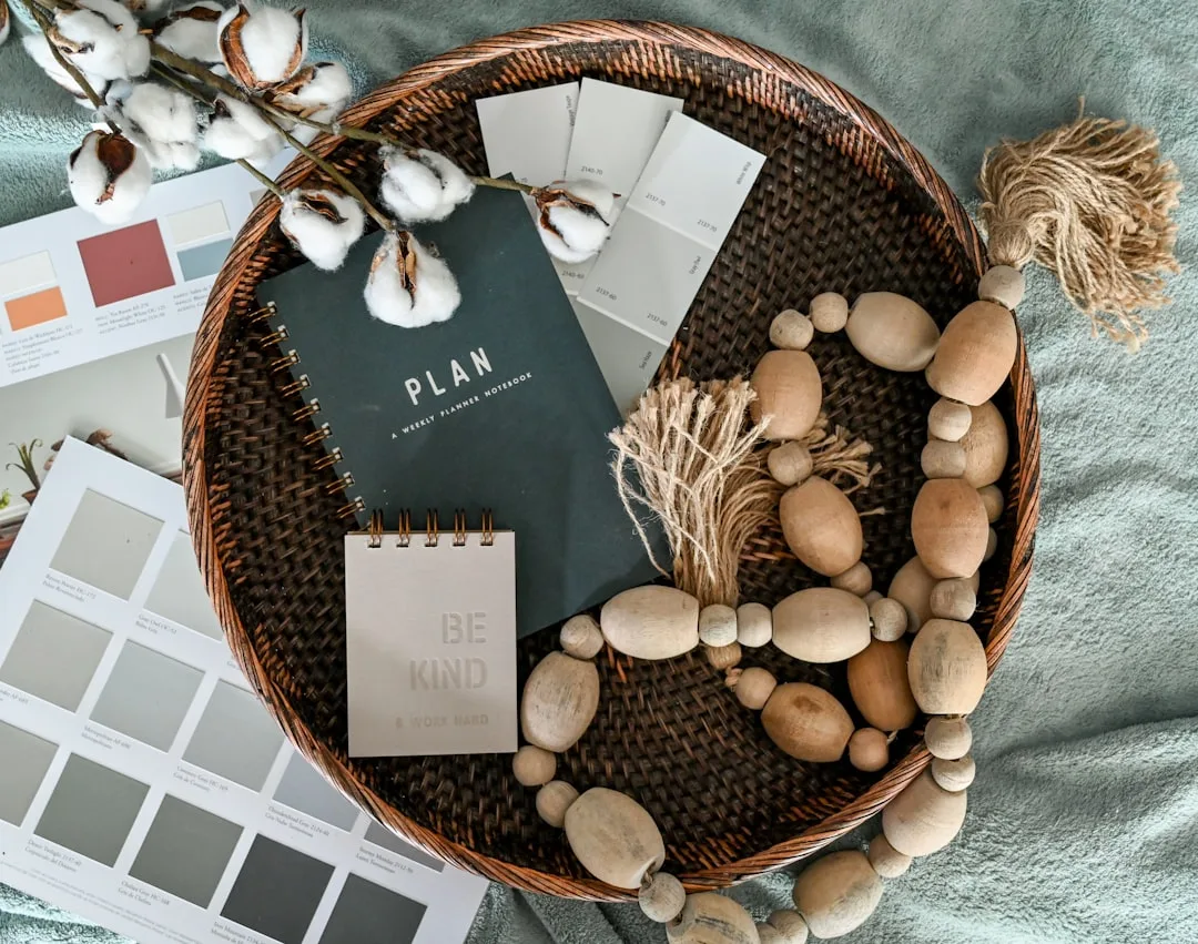 Farmhouse color palette swatches with neutral paint chips, wooden beads, cotton stems and planner notebook in wicker tra