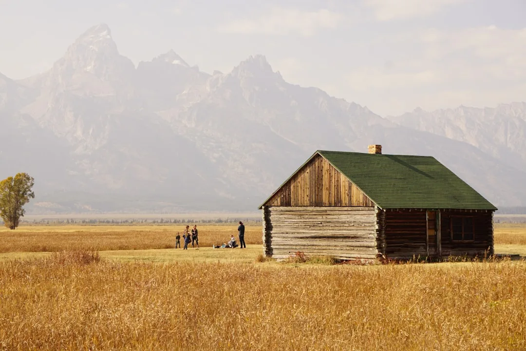 Rustic log cabin with green roof on golden prairie with Grand Teton mountains in background, Yellowstone region