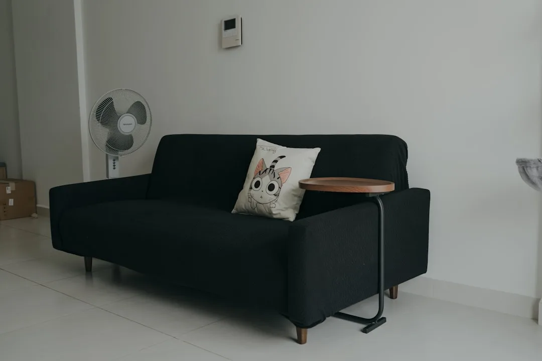 Black sofa with C-shaped side table positioned at armrest showing gap spacing in minimalist living room
