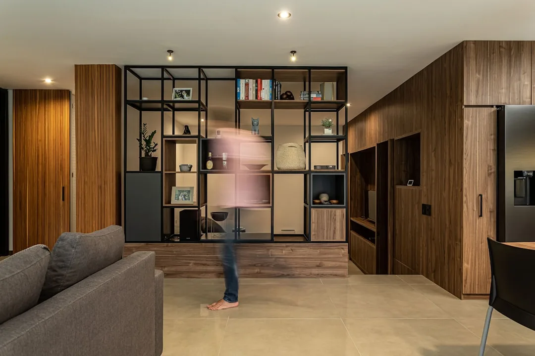 Floor-to-ceiling black metal shelving unit with layered decor styling in modern living room with warm wood panels