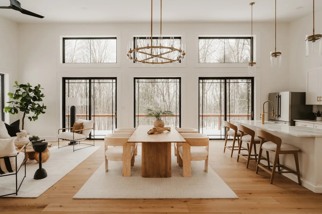 Modern farmhouse open-concept dining room with natural wood table, white oak floors, black-framed windows, and brass cha