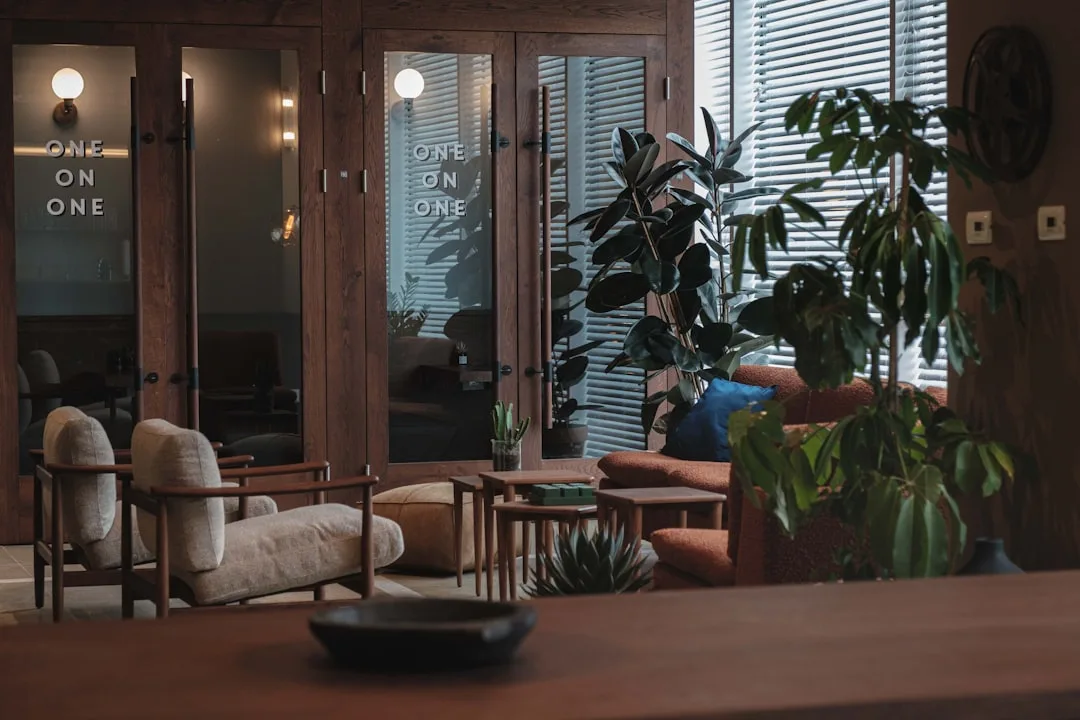 Moody interior lounge with mix of cream bouclé armchair and rust sofa beside rubber plant and wooden glass doors