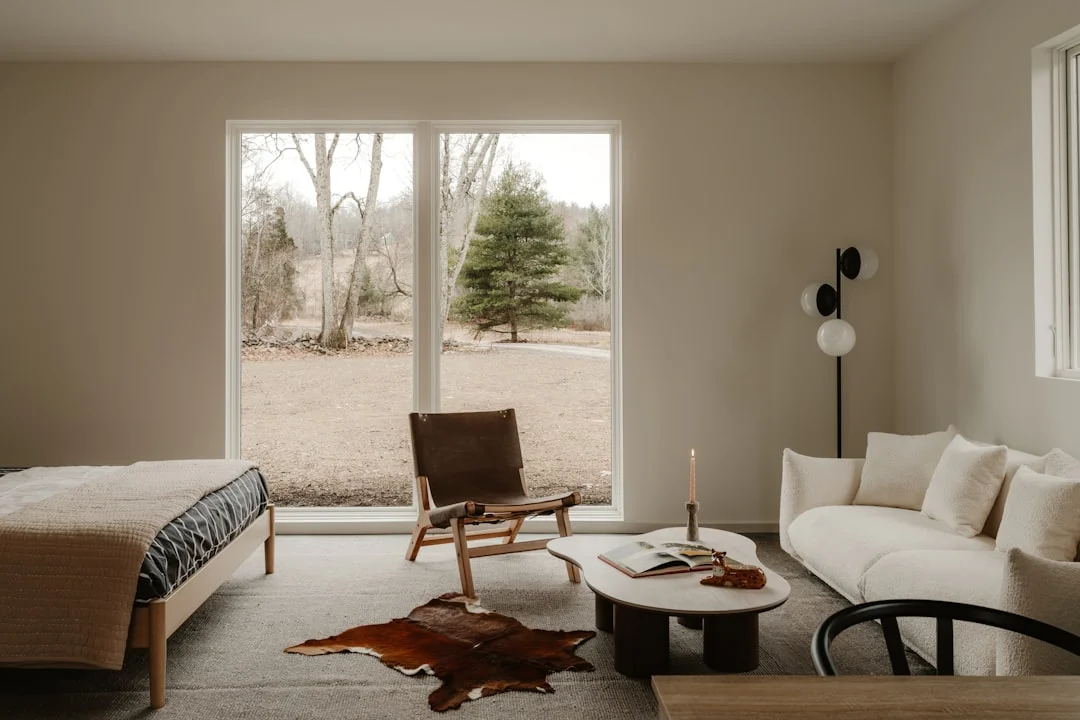 Minimalist studio bedroom with leather chair, boucle sofa, cowhide rug and warm layered lighting
