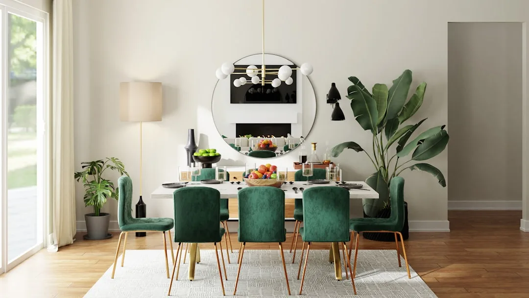Modern dining room with green velvet chairs, marble table, round mirror, and large indoor plant defining open-plan space