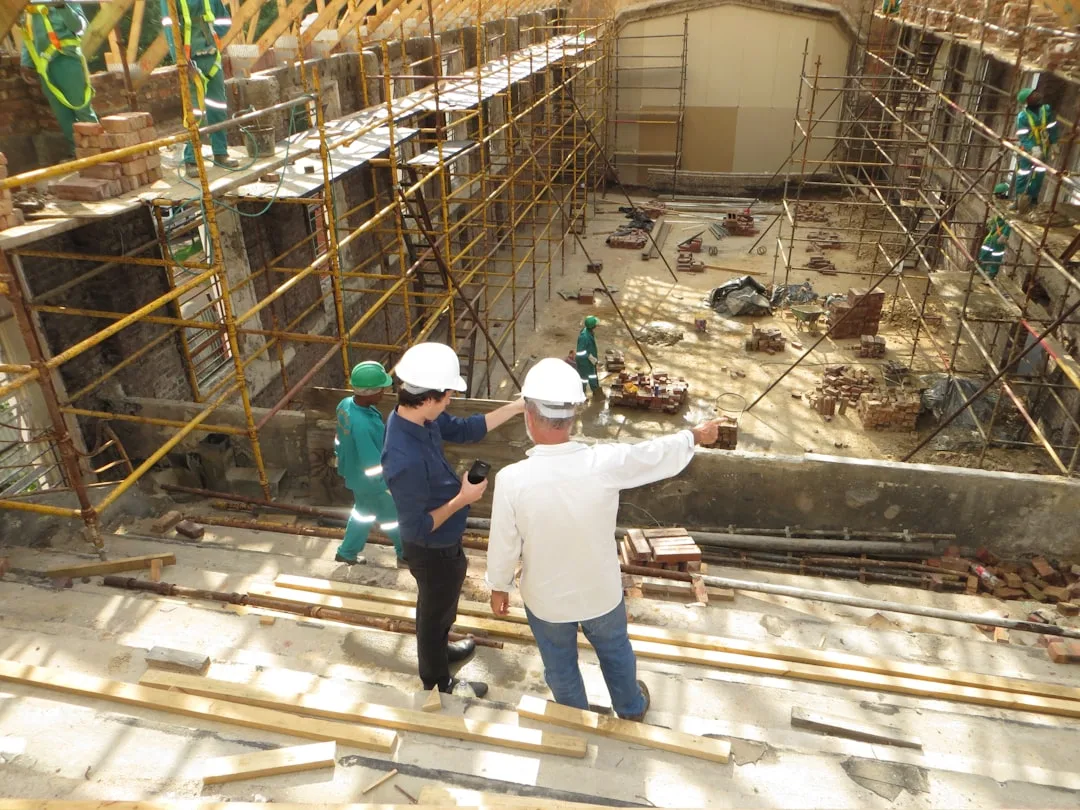 Construction inspectors in hard hats reviewing renovation permits at active building site with scaffolding