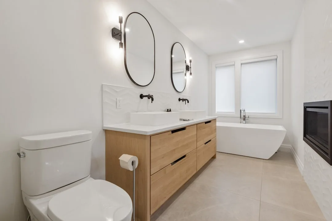 Modern bathroom with wood vanity, dual vessel sinks, wall-mount faucets, freestanding tub, and fireplace