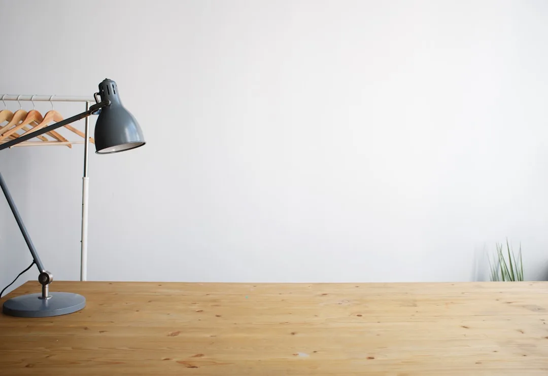 Gray adjustable desk lamp on wooden desk against white wall illustrating desk lighting setup
