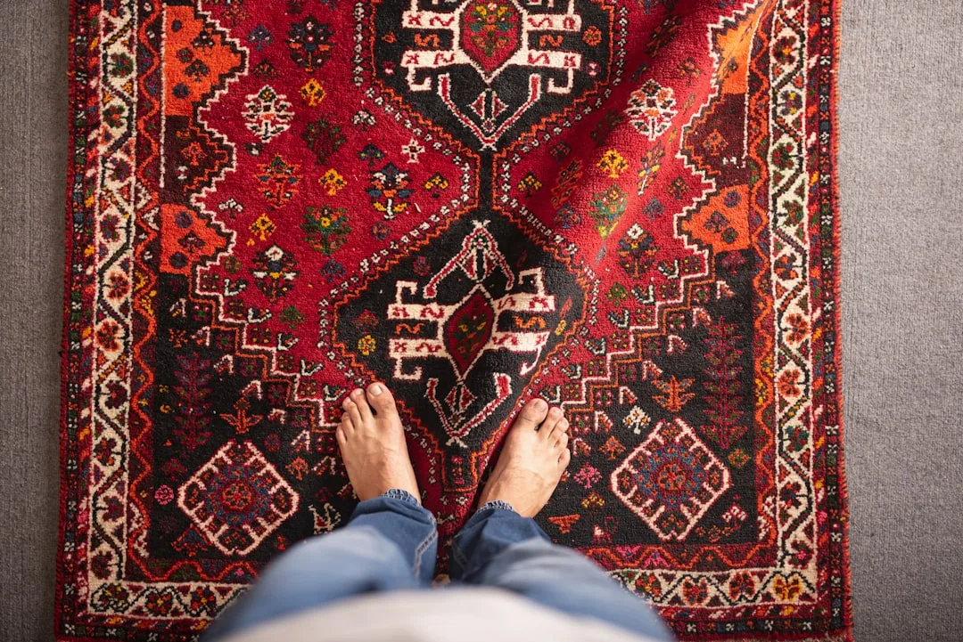 Bare feet standing on a vibrant red Persian rug with intricate patterns, illustrating rug sizing in a living room