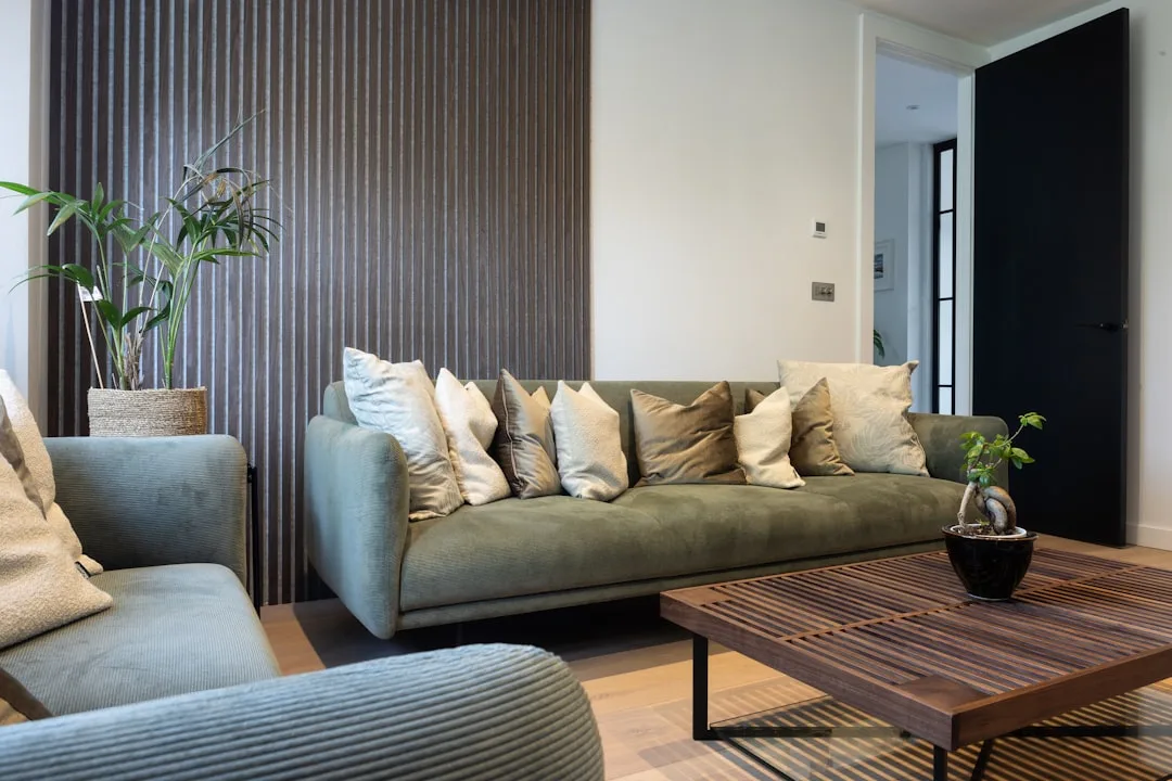 Modern living room with dark wood slat wall panel, olive green sofa, wooden coffee table and coordinated neutral tones