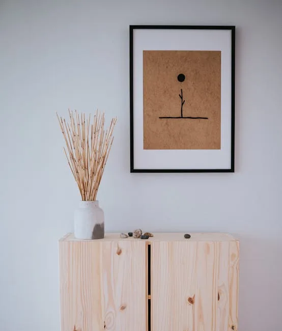 Japandi-style wooden cabinet with white ceramic vase, dried branches, and minimalist framed botanical art on white wall