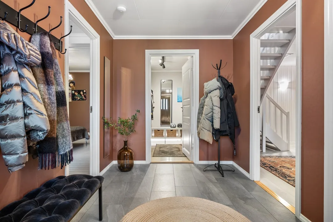 Fall entryway with terracotta walls, puffer jackets on hooks, velvet bench, woven rug, and mixed textures for a cozy aut