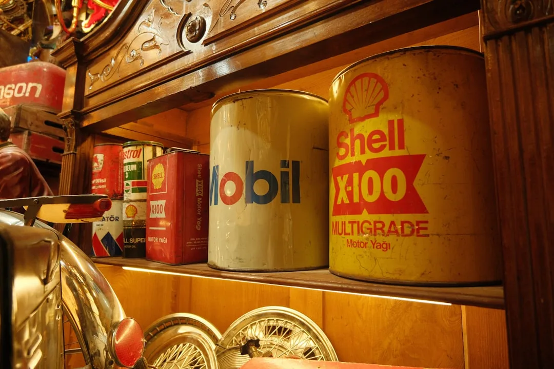 Vintage Mobil and Shell X-100 Multigrade motor oil cans displayed on wooden shelves alongside antique automotive collect