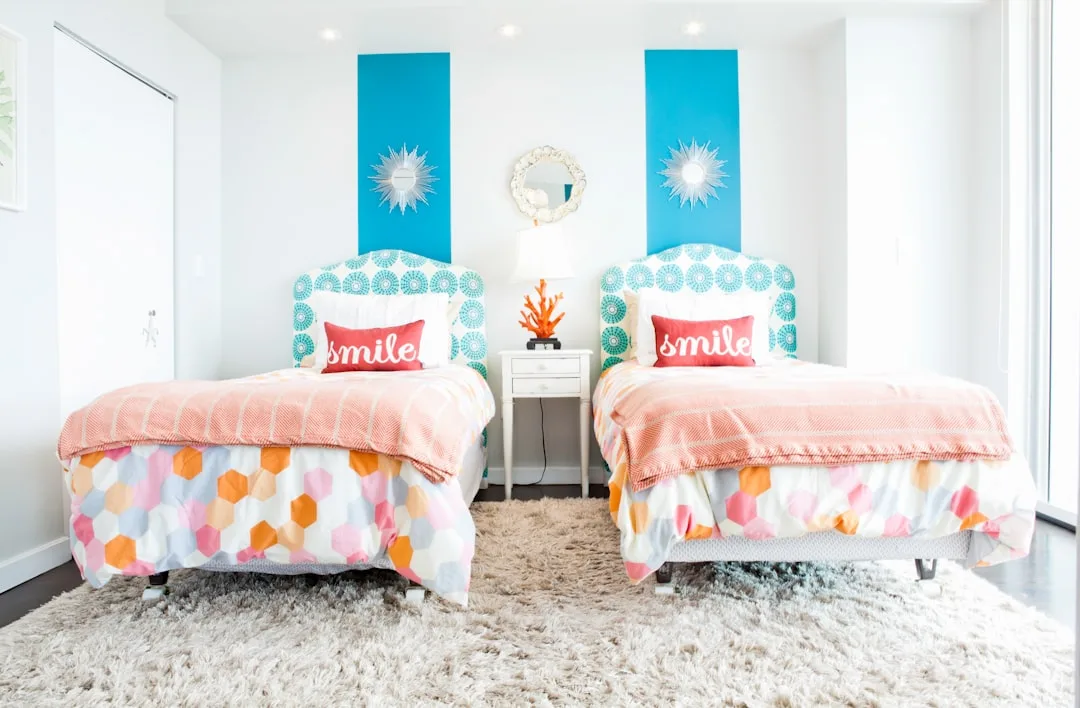Twin beds with colorful hexagon bedding and teal upholstered headboards in a bright white shared kids bedroom