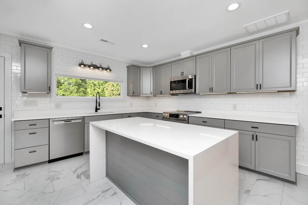 Modern kitchen with gray shaker cabinets, matte black hardware, white quartz countertops, and subway tile backsplash