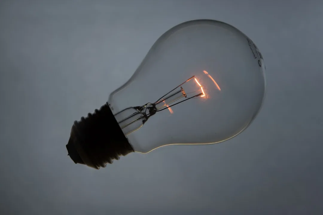 Clear incandescent light bulb with glowing filament against gray background, showing internal wire structure