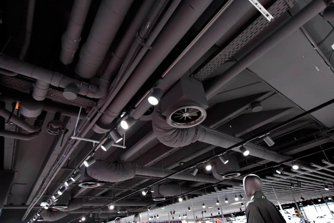Exposed ceiling ventilation ducts, HVAC pipes, and track lighting in a modern commercial interior space