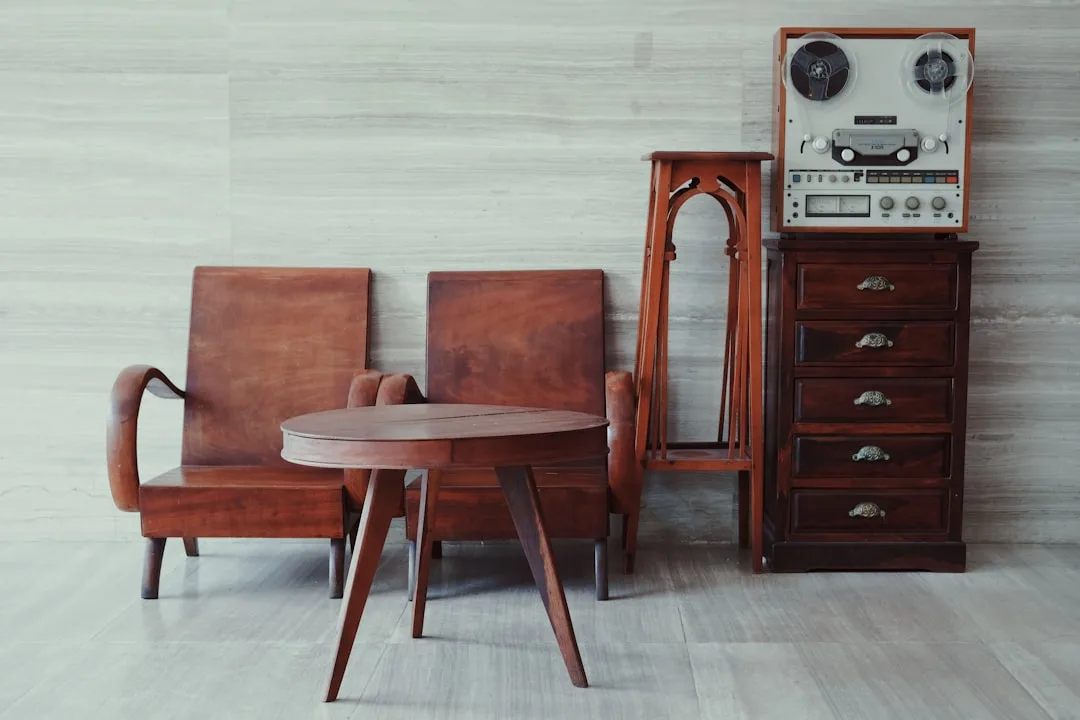 Mid-century vintage wooden armchairs and round coffee table with reel-to-reel tape recorder on dark wood dresser