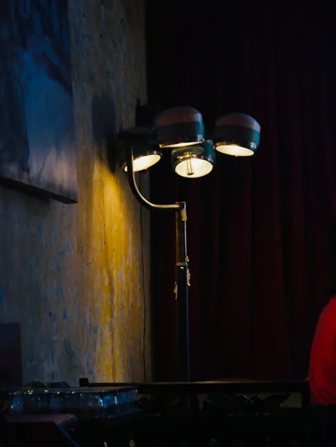 Vintage three-head floor lamp with glowing bulbs on a dark stage beside a textured wall and red curtain