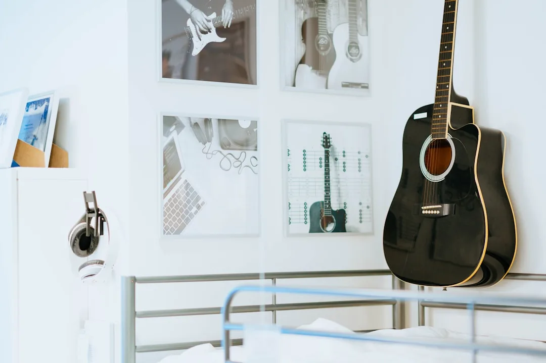 Dorm room wall with framed music art gallery layout, black acoustic guitar leaning against white wall