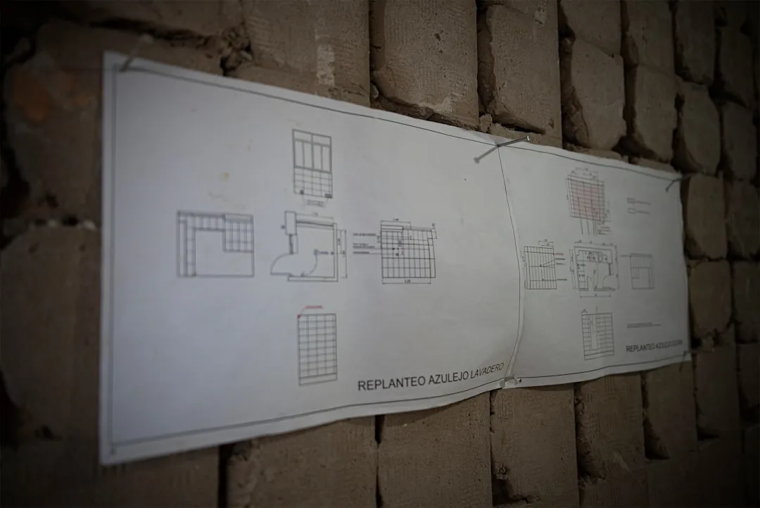 Construction blueprint pinned to exposed brick wall showing tile layout plans labeled Replanteo Azulejo Lavadero
