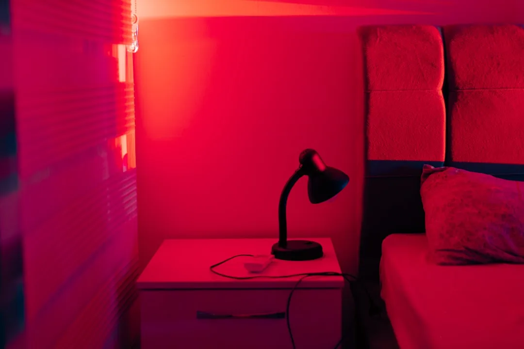 Bedroom nightstand bathed in intense red light with a small desk lamp, illustrating stimulating red light before bed