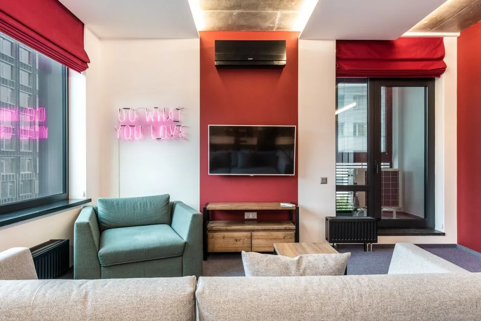 Bold red accent wall living room with neon 'Do What You Love' sign, teal armchair and grey sofa — baddie room aesthetic