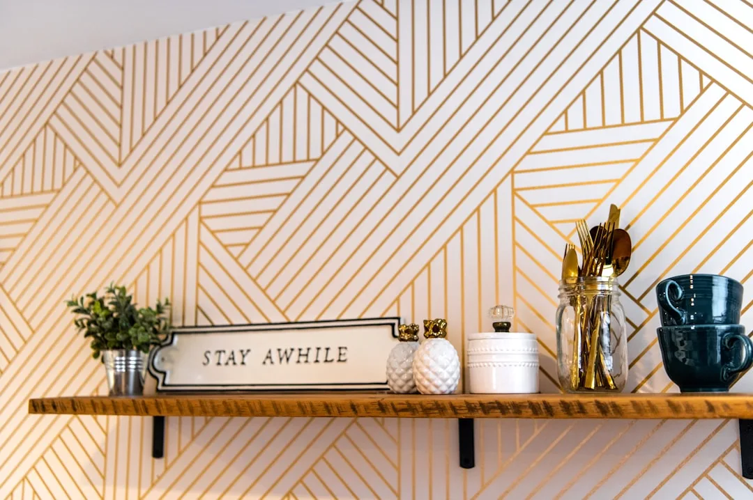 DIY gold geometric accent wall with white and gold stripe pattern behind a rustic wooden shelf with decorative items