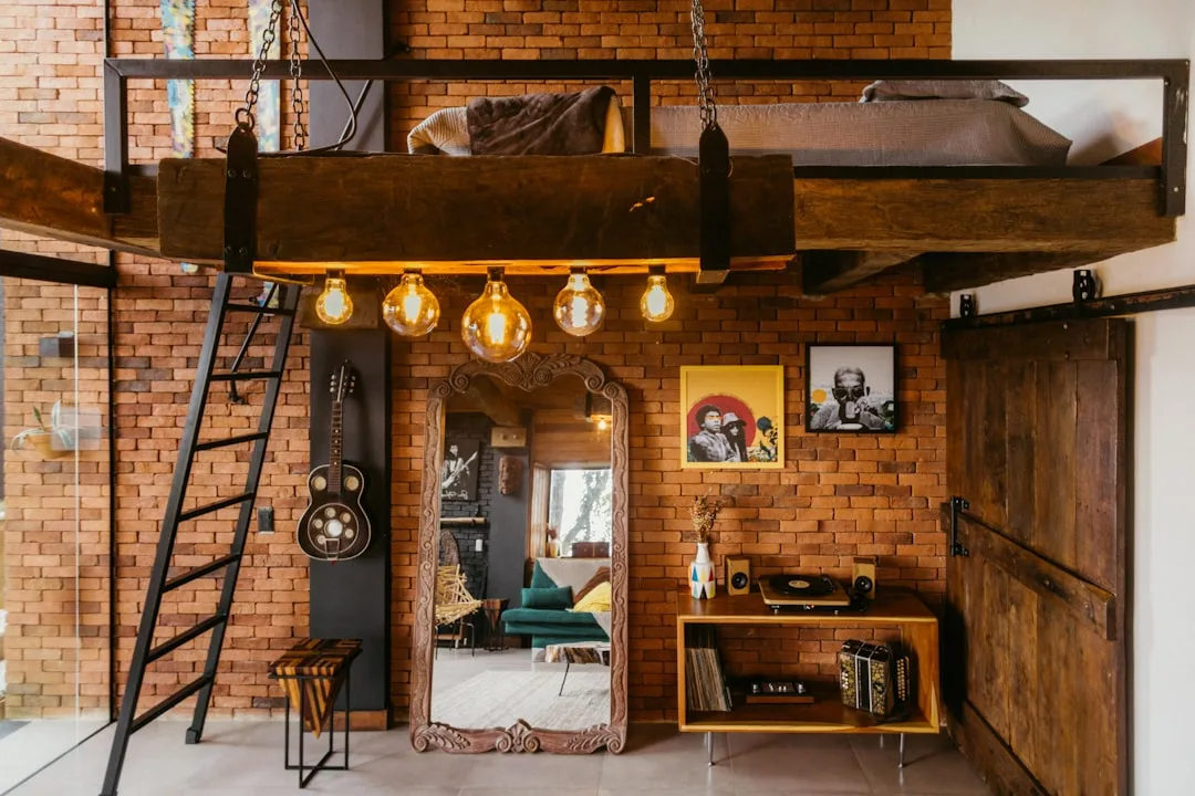 Industrial loft with exposed brick wall, Edison bulb pendant lights, guitar, vinyl record player, and mezzanine bed on c