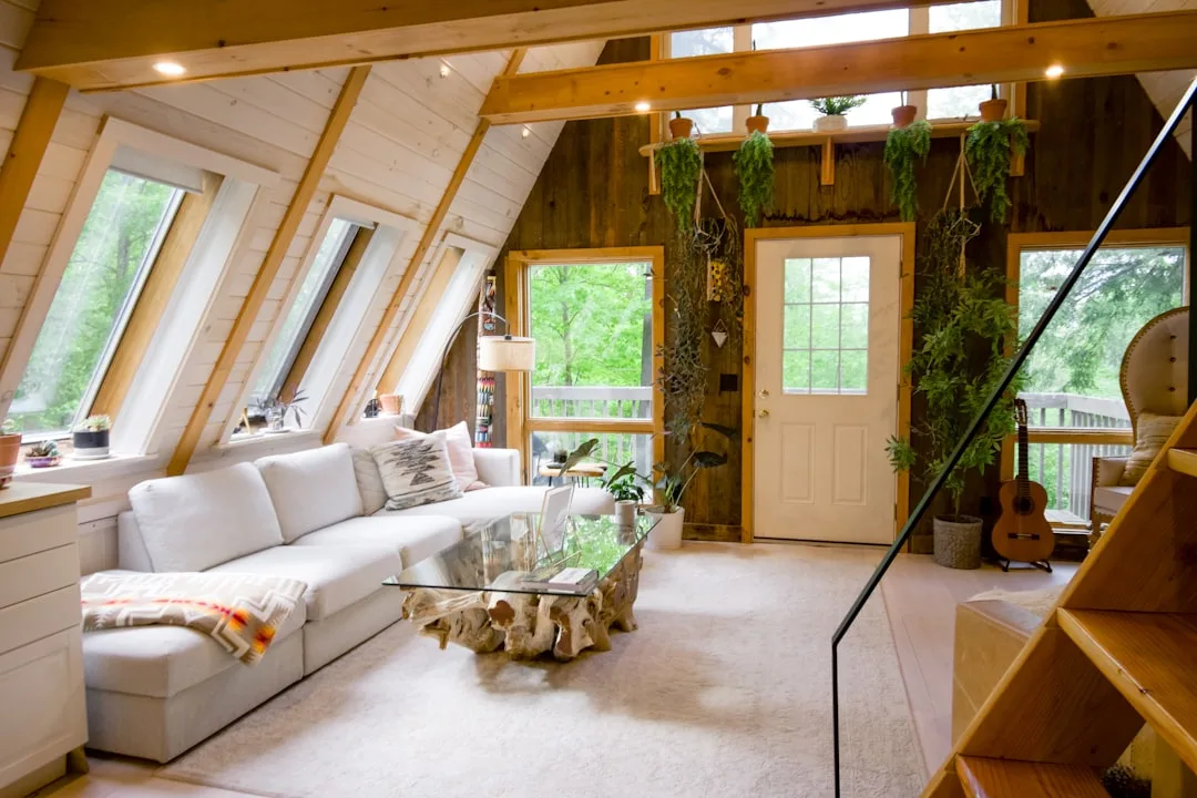 A-frame attic conversion living space with sloped wood beam ceiling, skylights, white sofa and hanging plants