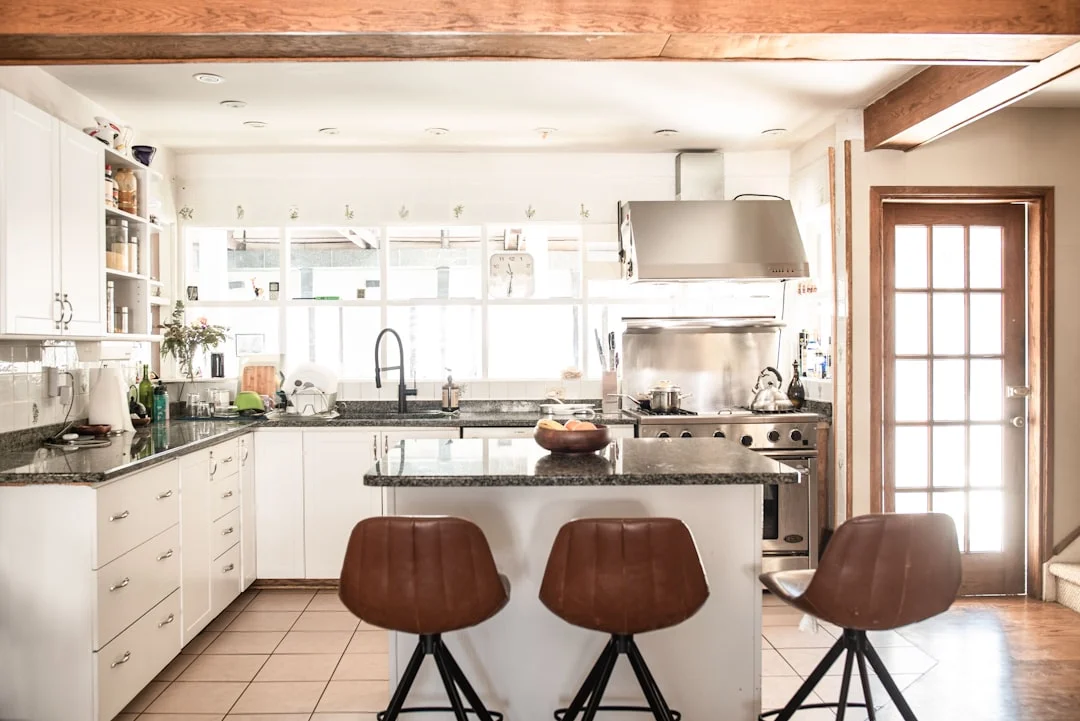 White kitchen with granite island, bar stools, stainless steel range and hood, natural light