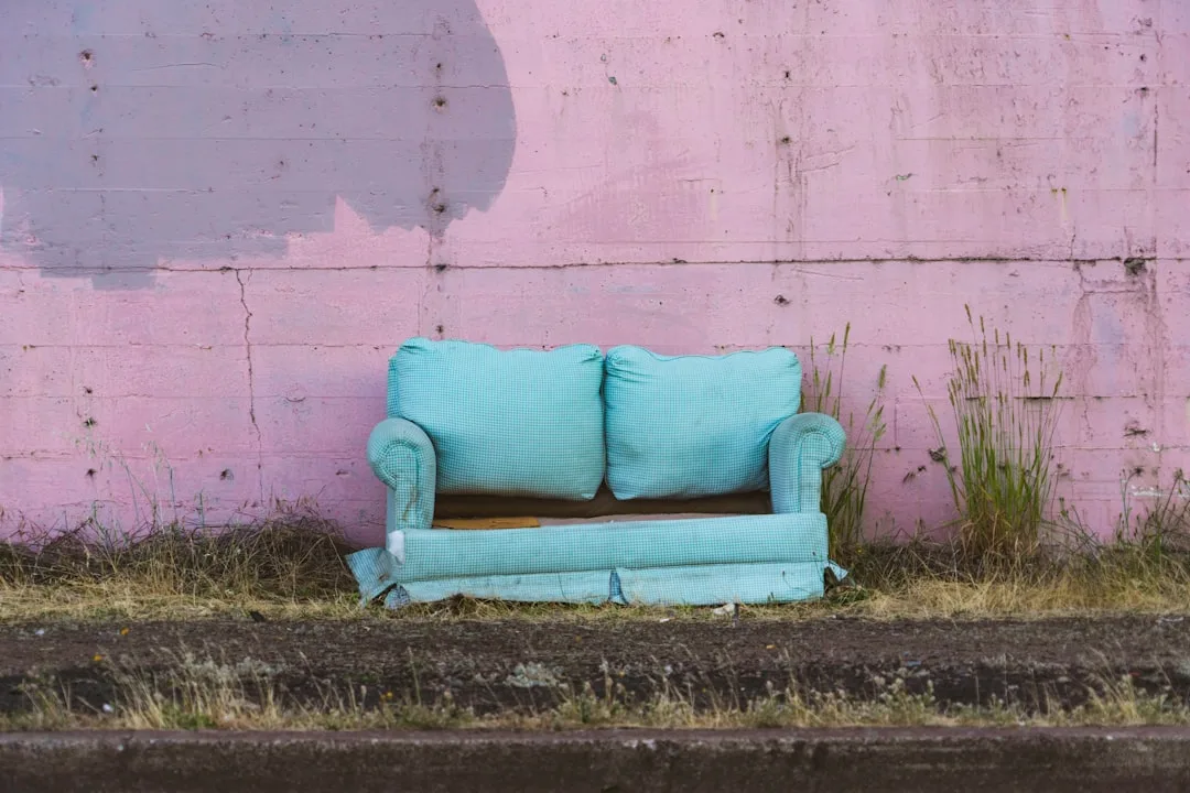 Abandoned teal loveseat with oversized back cushions against a pink wall, illustrating furniture proportion and visual w