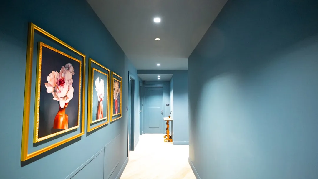 Hallway gallery wall with three gold-framed floral portrait artworks on blue wall in modern corridor