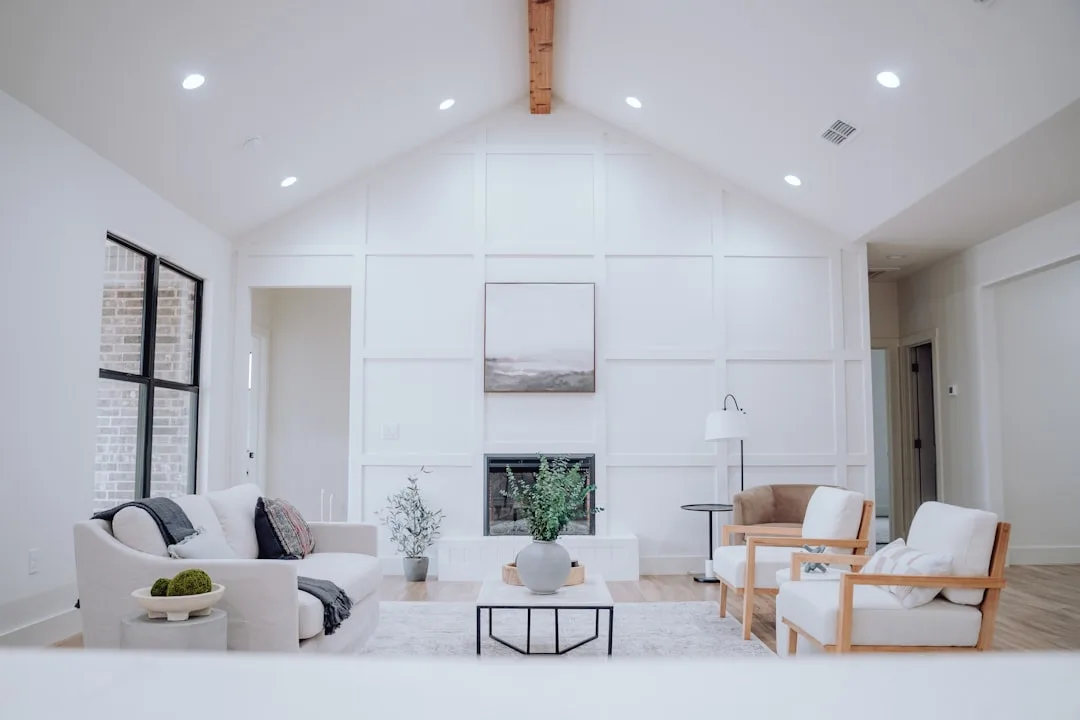 Bright modern farmhouse living room with vaulted ceiling, white sofa, wooden accent chairs, and fireplace focal wall