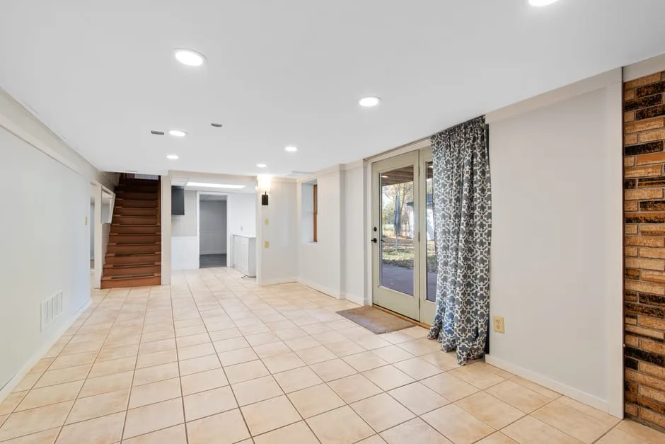 Open basement entry zone with tile flooring, glass door, curtains, staircase, and recessed lighting