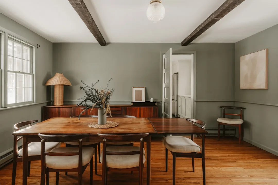 Mid-century modern dining room with floating table pulled from sage green walls and exposed wood ceiling beams