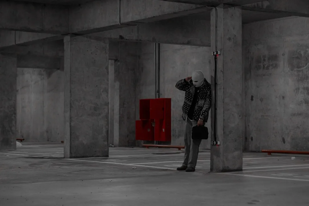Person standing in empty raw concrete basement parking structure with exposed columns and infrastructure before renovati