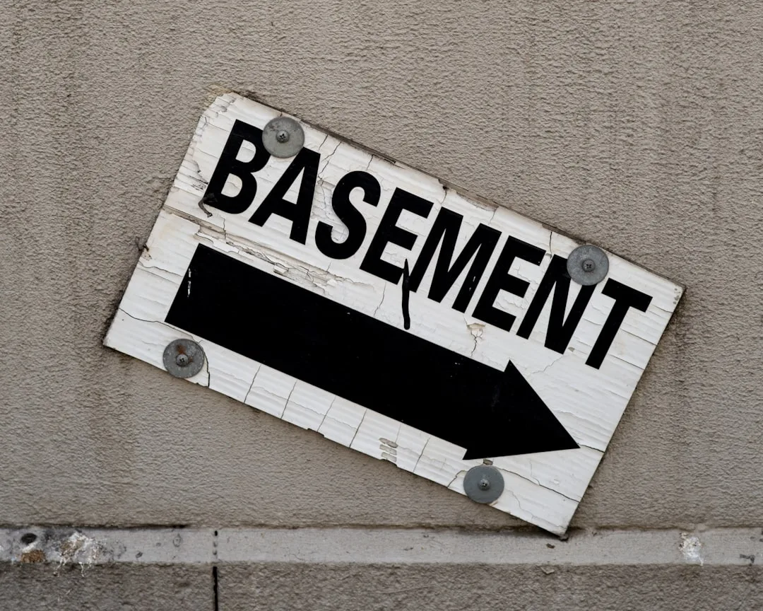 Weathered white wooden basement directional sign with black arrow mounted on stucco wall