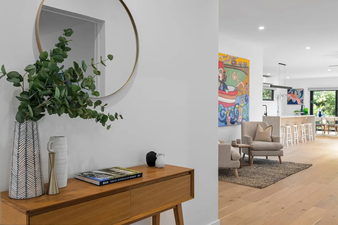 Mid-century wooden console table with vases and books in modern hallway entry leading to open-plan living room