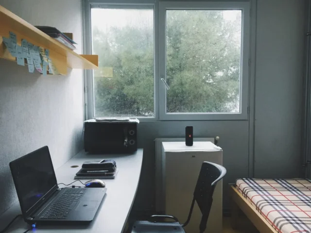 Cluttered dorm room with laptop desk, microwave, m