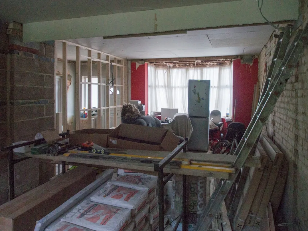 Home renovation in progress showing exposed timber stud wall framing, brick walls, and construction materials before lay