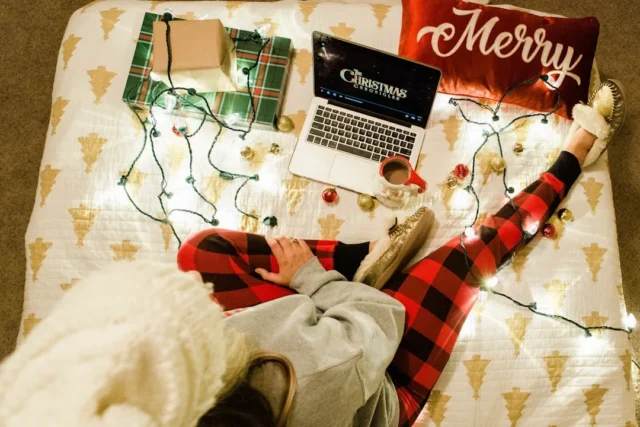Person in plaid pajamas on bed with Christmas ligh
