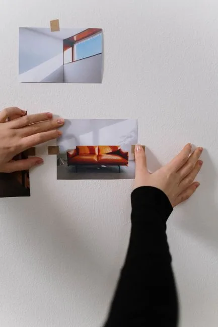 Hands pinning interior design mood board photos to white wall with tape for room planning