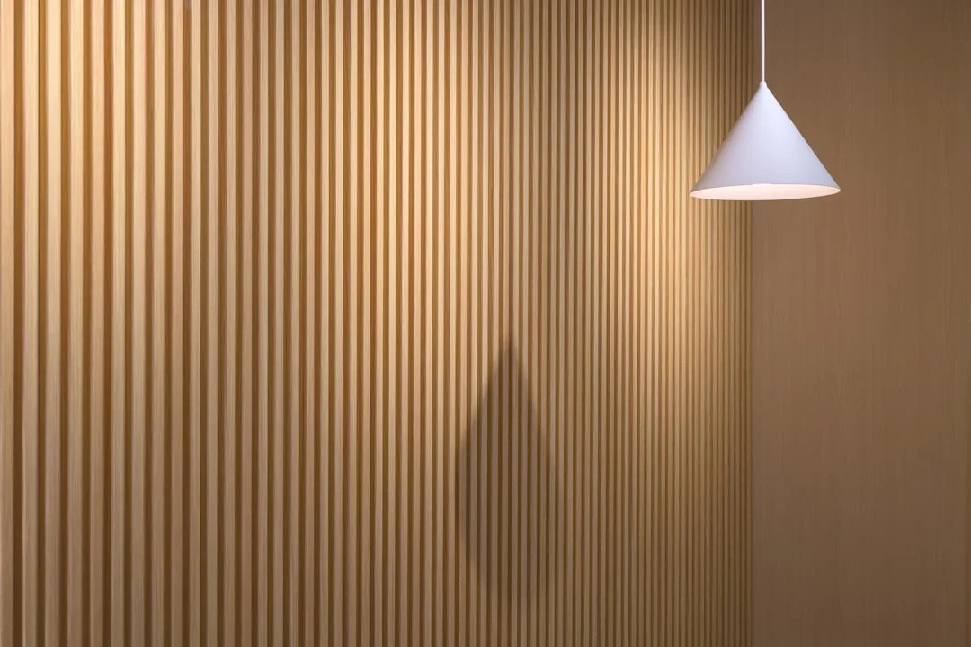 Vertical wood slat wall panel system with warm oak finish and white cone pendant lamp in modern interior