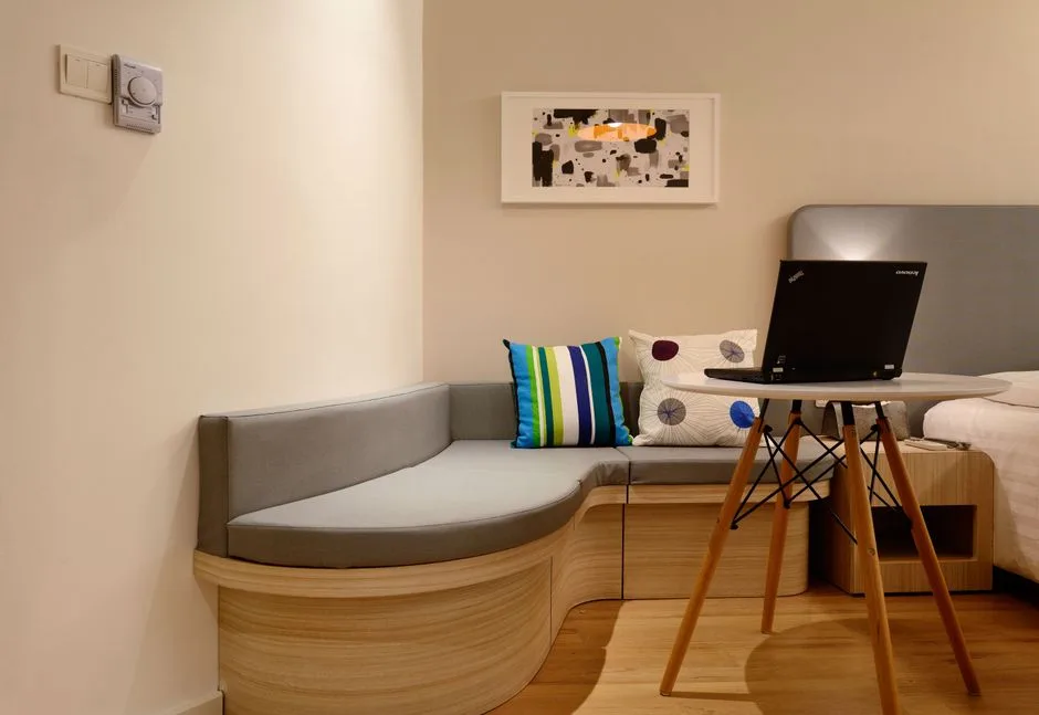 Compact hotel room with gray curved bench, colorful striped cushion, and neutral warm beige walls showing color balance