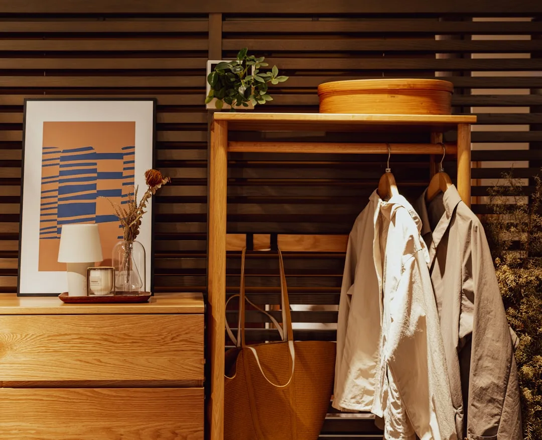 Organized open wardrobe with wooden rack, hanging jackets, tote bag, and dresser styled like a retail display
